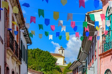 Aziz John şenlikleri için bayraklarla süslenmiş sokak koloni tarzı evler ve Ouro Preto şehrinin arka planında bir kilise var.