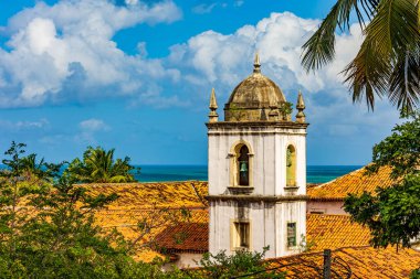 Arkasında deniz olan Olinda şehrinin bitki örtüsünün ortasındaki tarihi barok kilise kulesi.