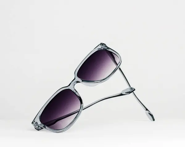 Beyaz arkaplanda sanatsal olarak sergilenen, saydam gri çerçeveli ve gradyan mor lensli büyük kare güneş gözlüğü. Yaz moda aksesuarları
