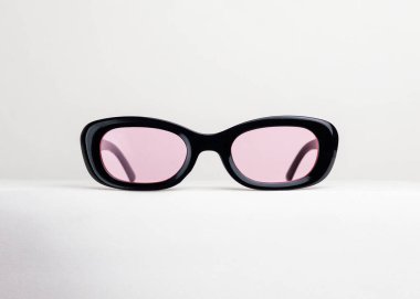Beyaz arka planda duran siyah çerçeveli ve pembe mercekli funky oval güneş gözlüğü.