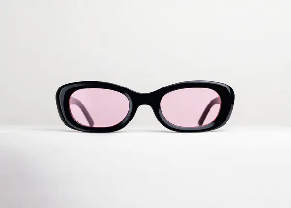 Beyaz arka planda duran siyah çerçeveli ve pembe mercekli funky oval güneş gözlüğü.