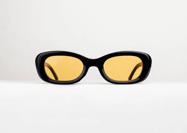 Siyah çerçeveli güneş gözlüğü ve beyaz arka planda sarı lens. Şık ve havalı. Güneş gözlüğü.
