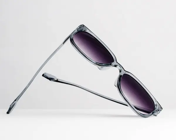 Şeffaf gri çerçeveli, modaya uygun güneş gözlükleri ve beyaz arka planda mor renkli lensler. Moda yaz aksesuarları