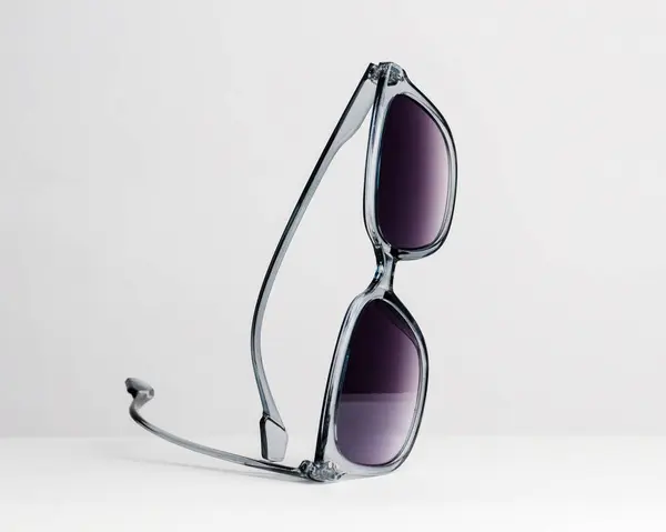 Sanatsal olarak beyaz arkaplanda güneş gözlüğü ve metin için kopyalama alanı gösterilir. Şeffaf gri çerçeveli ve gradyan mor lensli moda güneş gözlükleri.