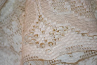 Zarif desenler ve dokular gösteren karmaşık beyaz dantel kumaşın ayrıntılı görüntüsü. Hassas tasarım zanaatkarlığı ön plana çıkarıyor, zarafet ve klasik cazibe katıyor..