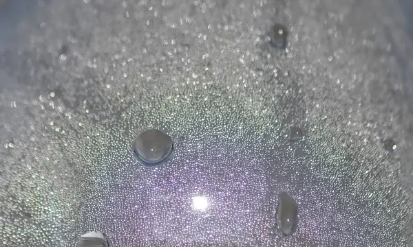 Yansıtıcı bir yüzeyde dinlenen su damlacıklarının yer aldığı makro fotoğrafçılık, yanardöner röfle ve karmaşık dokular sergiliyor, günlük basitlikte bir detay ve güzellik hissi uyandırıyor.
