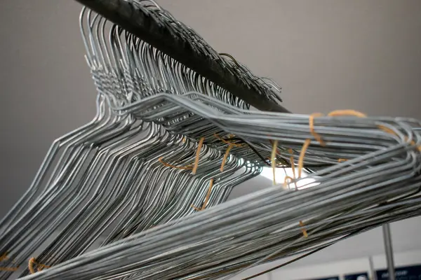 Askıda asılı duran metal elbise askılarının detaylı bir görünümü, genellikle çamaşırhanelerde veya depolama alanlarında görülür, organizasyonu, basitliği ve giysi bakımını sembolize eder.