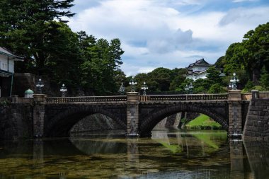 Bu çarpıcı görüntüde, Japonya, Tokyo 'daki İmparatorluk Sarayı' nın etrafını saran sakin sular üzerinde zarif bir şekilde uzanan görkemli bir köprü sahne alıyor.. 