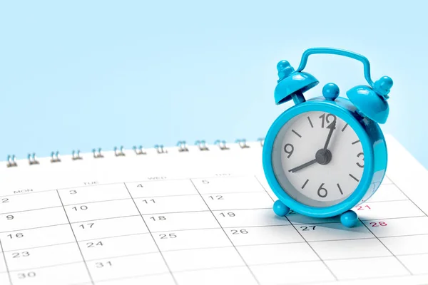 Blue alarm clock on a calendar with a blue background.