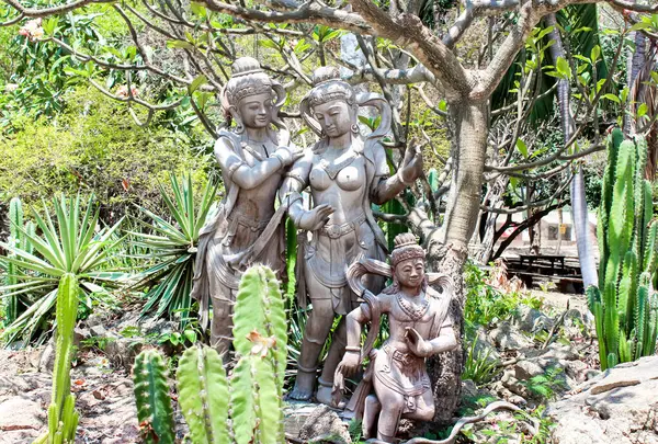 Canlı bir tropikal bahçede, süslü heykeller güneşli gökyüzünün altında yemyeşil bitkiler ve kaktüslerle çevrilidir.