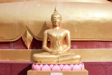 Altın Buda heykeli, altın ve kestane arkaplanlı dini bir tapınağın bir parçası olan pembe nilüfer tabanında oturuyordu..