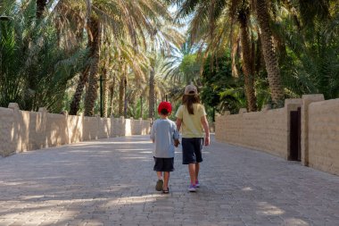 İki çocuk Al Ain Oasis 'te yürüyor, BAE, popüler bir turist mekanı. Vaha, sıcaktan korunmak için gölgeler ve serin bir kaçış sağlar. Bu da onu doğada dinlenmek için mükemmel bir yer yapar.