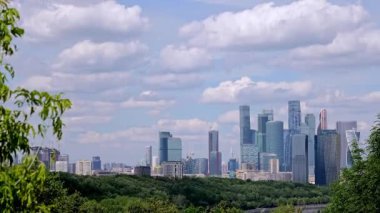 Vorobyovy Gory 'nin Moskova Nehri üzerindeki manzarası, yemyeşil ağaçlar ve mavi gökyüzündeki bulutlar. Moskova Nehri 'nin doğal güzelliği arka planda şehrin ufuk çizgisini tamamlar.