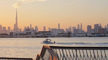Dubai 'de aktif eğlence: gün batımında Dubai Deresi' nde motorlu bir teknenin arkasında wakeboard sürmek. Arka plandaki Dubai silueti şehrin enerjisini ve açık hava yaşam tarzını ön plana çıkarıyor. 8 Ocak 2025, Dubai, BAE