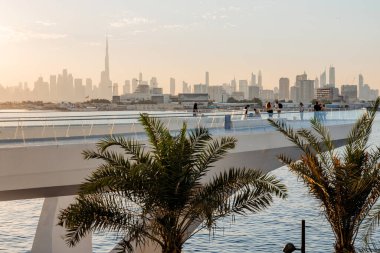 Dubai şehir merkezi ufuk çizgisinin güzel günbatımı manzarası ve Dubai Creek kanalı sakin bir akşam atmosferi, modern mimarisi, huzurlu su yansımaları, insan siluetleri. 8 Ocak 2025, Dubai, BAE