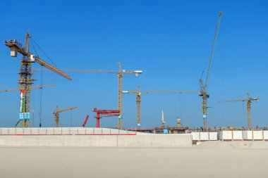 Mavi gökyüzünün altındaki inşaat alanında vinçler. Görüntü, ağır makineler ve yapısal büyümeyle çağdaş inşaat projelerinin ölçeği ve yoğunluğunu vurguluyor. 24 Ocak 2025, Dubai, BAE
