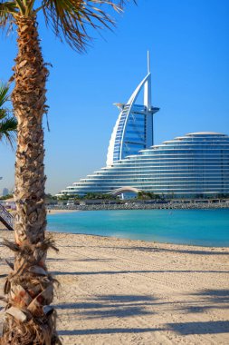 Burj Al Arab ve Jumeirah Beach Hotel, Dubai, BAE 'deki sakin turkuaz sudan görüldü. İkonik mimari, tatil köyü lüksü ve kıyı zarafetinin yer aldığı modern bir gökyüzü.