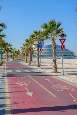 Dubai sahilinin yanındaki palmiye ağaçlarının arasından geçen açık işaretli kırmızı bisiklet yolu. Aktif bir kıyı yaşam tarzı için bisiklet, koşu, yürüyüş ve keyif için popüler bir nokta