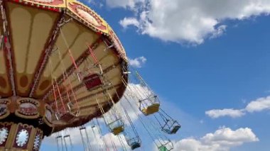 Tüylü bulutlara karşı düzenlenen bir yaz festivalinde geriye doğru sallanma hareketi. Bu nostaljik çekim panayırlarda gözde, heyecan ve kaygısız anlar sunuyor.