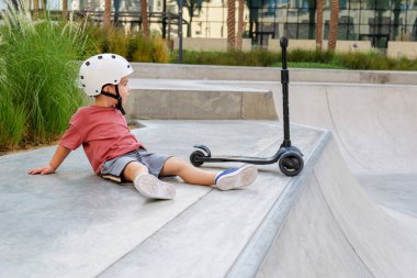 Kask takan ve kaykay parkında scooterıyla dolaşan küçük bir çocuk. Yüksek kalite fotoğraf