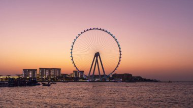 Bluewaters Adası 'nın panoramik günbatımı manzarası ve Dubai Marina dönme dolabı plajdan, sakin şehir silueti, seyahat.