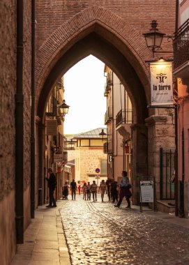 İnsanlar gün batımında İspanya 'nın Teruel kentindeki El Salvador Kulesi' ne doğru kemer altında yürüyorlar..