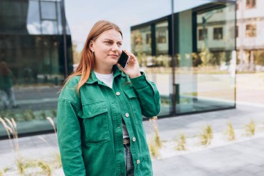 Güzel, sıkıcı kızıl saçlı kadın akıllı telefonuyla konuşuyor. Şehir caddesinde akıllı telefon kullanan bir kadın. Kentsel yaşam tarzı konsepti