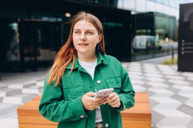 Genç mutlu iş kadını şehirde gülümsüyor ve akıllı telefon kullanıyor. Ofise giden güzel bir kadın akıllı telefonuyla internetten bilgi arıyor. İş, eğitim kavramı