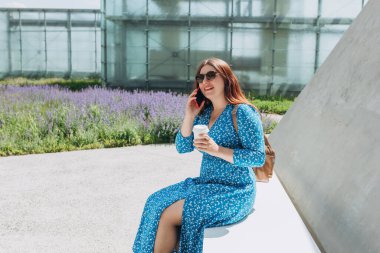 Genç kızıl saçlı kadın şehirde cep telefonuyla konuşuyor. Akıllı telefondan arkadaşıyla konuşan mutlu bir kadının portresi. Telefon iletişimi. Kentsel yaşam tarzı konsepti.