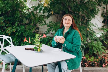 Kafeteryada çay içen güzel bir kadının portresi. Kafede kahve içen genç kızıl saçlı kadın, mutlu duygular..