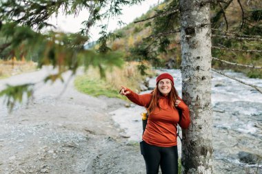 Kırmızı şapkalı, ormanda yürüyüş yapan mutlu kızıl kadın. Nehrin kenarında duran ve dağları işaret eden maceraperest kadınlar. Özgürlük ve aktif yaşam tarzı kavramı