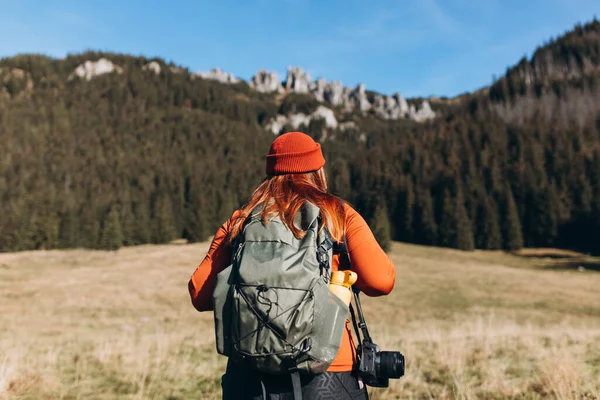 緑のバックパックを身に着けているスタイリッシュな女性と山の景色を見ながら 自然の中でリラックスした赤い帽子の背面ビュー 旅と放浪の概念 — ストック写真