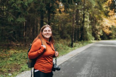 Sonbahar ormanlarında yürüyüş yapan turist kadın. Aktif yürüyüş kıyafetleri içinde mutlu kızıl saçlı insan doğanın gerisinde yürüyor. Seyahat ve aktif yaşam tarzı kavramı.