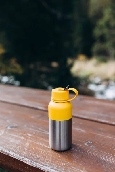 stock image A vacuum theroms stands on a tree desk in the wild. Hiking equipment on footpath in woodland. Travel outdoor concept