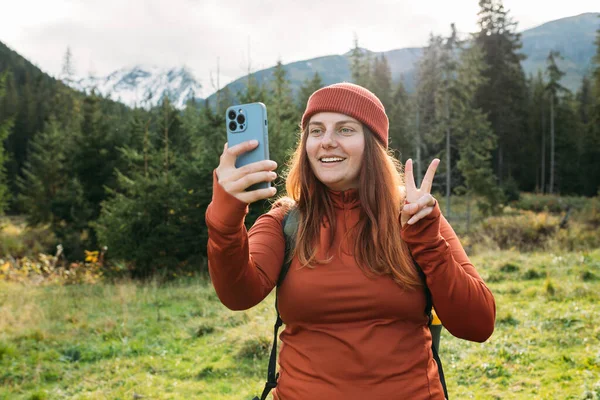 帽子の女性は写真を撮るために電話を使用し 山の背景に自宅から自撮りやビデオ通話を家族にします 旅と放浪の概念 — ストック写真