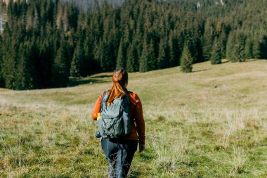 Doğada dinlenirken dağ manzarasında yeşil sırt çantası takan şık bir kadının arka planı. Seyahat ve seyahat tutkusu konsepti