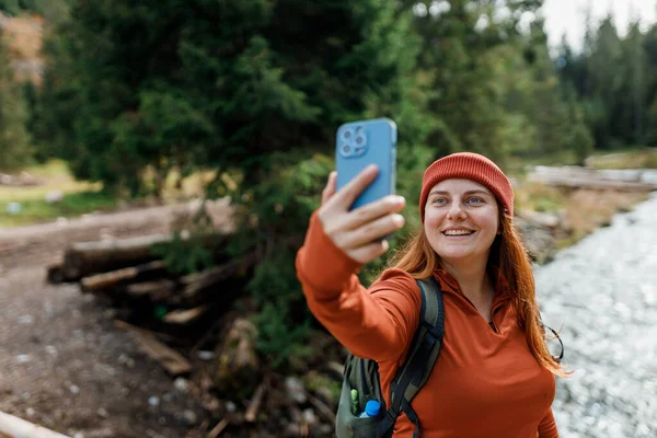 帽子の女性は写真を撮るために電話を使用し 山の背景に自宅から自撮りやビデオ通話を家族にします 旅と放浪欲の概念 寒気の瞬間 — ストック写真