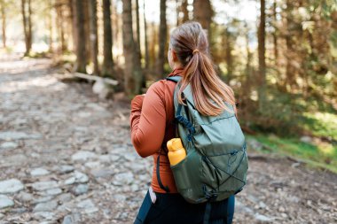 Doğada dinlenirken, dağ manzarasında yeşil sırt çantalı bir kadının arka görüntüsü. Sonbahar ormanlarında tek başına yürüyüş yapan bir turist. Aktif yürüyüş kıyafetleri içinde doğa üzerinde yürüyen biri.