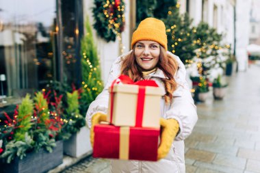 Hediye kutularını elinde tutan ve kış caddesinde gülümseyen mutlu, genç ve heyecanlı bir kadın. Kış tatili indirimi. Alışveriş, tatil ve noel kavramı.