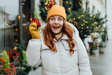 Bir kadın kışın dışarıda bir Noel hediyesi tutuyor. Kar yağışı. Firavun ağacı, çelenk arka planda. Alışveriş, tatil ve Noel kavramı.