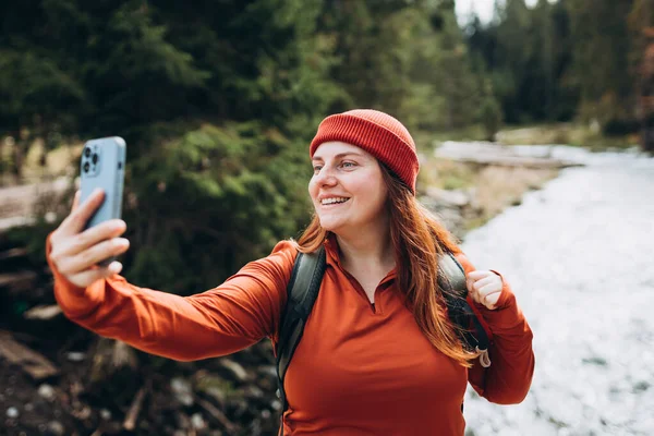 帽子の女性は写真を撮るために電話を使用し 山の背景に自宅から自撮りやビデオ通話を家族にします 旅と放浪欲の概念 寒気の瞬間 — ストック写真