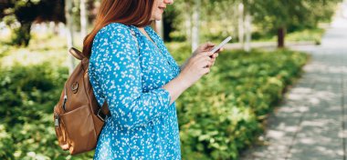 Güzel, şık bir kadın yaz günü şehirde yürüyor ve elinde akıllı bir telefon tutuyor. Telefon iletişimi. Şehir yaşam tarzı konsepti. Gezgin, sosyal ağları kontrol et