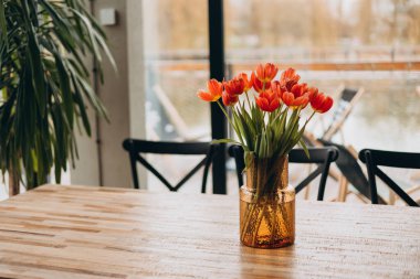 Sarı geometrik bir vazoda kırmızı laleler evdeki ahşap bir masada duruyor.