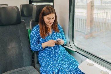 Akıllı telefonlu genç bir kadın trende seyahat ediyor. Cep telefonu kullanan mutlu kadınlar. Demiryolu taşımacılığı kavramı