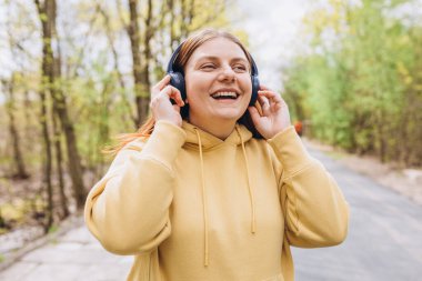 Doğa arka planında kablosuz kulaklıklardan müzik dinleyen mutlu bir genç kızın portresini yakın plan çek. Müzik aşığı müziği seviyor.