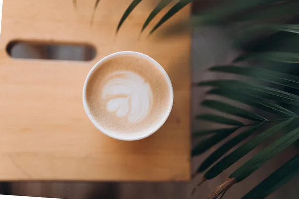 Top view of a paper cup of coffee with latte art on wooden table. Street coffee, top view. Cup coffee in palm branches and leaves