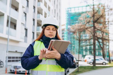 Beyaz kasklı ve güvenlik yeleği giyen genç mimar kadın dijital tablet kullanıyor. Kadın inşaat mühendisi. Mühendislik uygulaması
