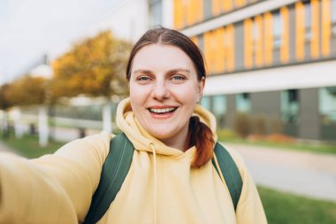 Gündelik giysiler içinde güzel bir kadın şehir caddesinde akıllı telefonunu kullanıyor. Genç hippi kentin arka planında selfie çekiyor. Kameraya bakıp gülümse. Seyahat ve aktif yaşam konsepti.