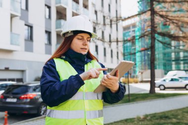 Young architect woman in white hardhat and safety vest using digital tablet. Female construction engineer. Engineering application