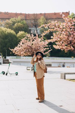 Moda kıyafetleri içinde gülümseyen güzel bir hippi kadın. Sokakta poz veren kaygısız seksi kadın. Açık havada pozitif model. Güneş gözlüğü ve şapkayla neşeli ve mutlu